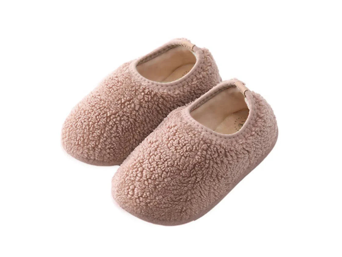 Ein Paar komfortable, hellrosa Kinderhausschuhe aus weichem Teddy-Stoff vor weißem Hintergrund.